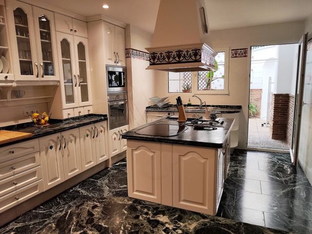 Cocina común de estilo tradicional, con muebles blancos, isla central y campana