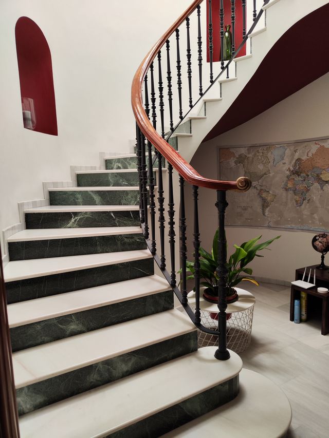 Arranque de la escalera en planta baja, con peldaños de mármol y barandilla de forja