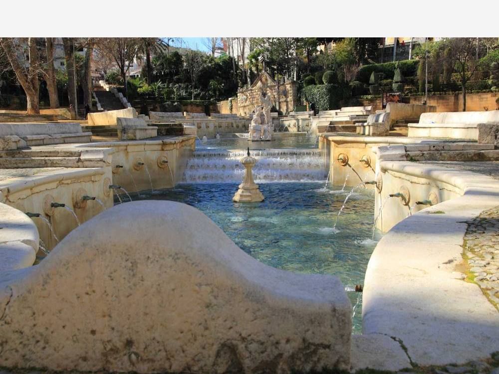 Fuente monumental de piedra con estanques escalonados, caños y surtidores entre árboles