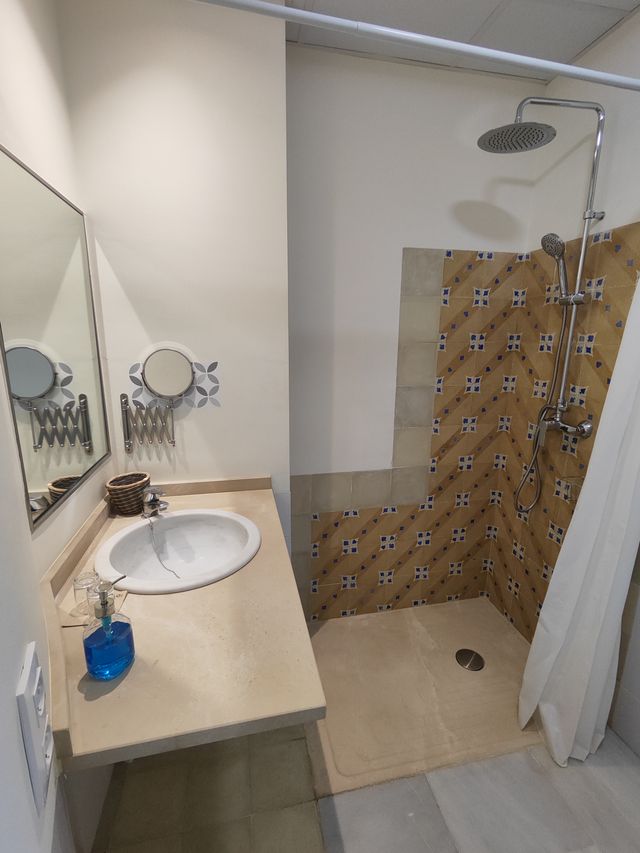 Baño de la habitación accesible, con ducha a ras de suelo, lavabo y alicatado de baldosa artesanal