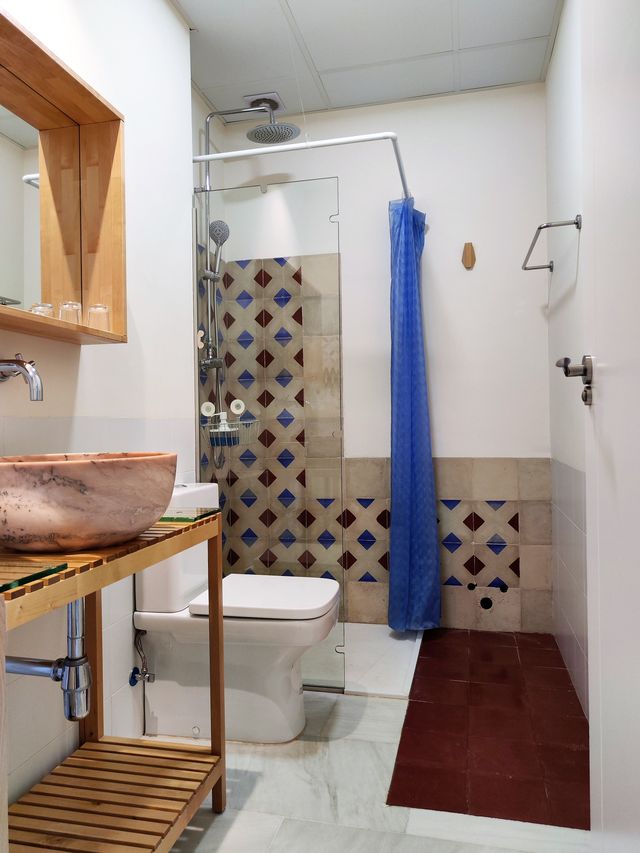 Baño completo del apartamento, con ducha, lavabo de piedra sobre mueble de madera y alicatado artesanal