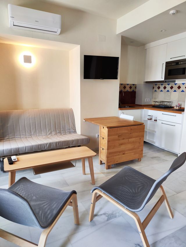 Zona de estar del apartamento con sofá-cama, dos butacas y la cocina-comedor al fondo