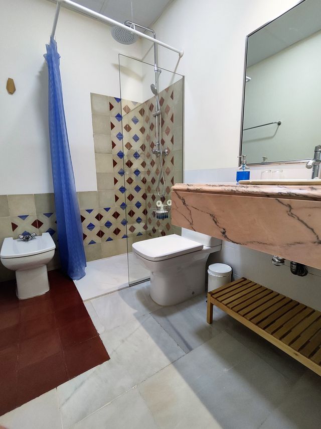 Baño completo con ducha, lavabo de mármol sobre mueble de madera y alicatado de baldosa artesanal