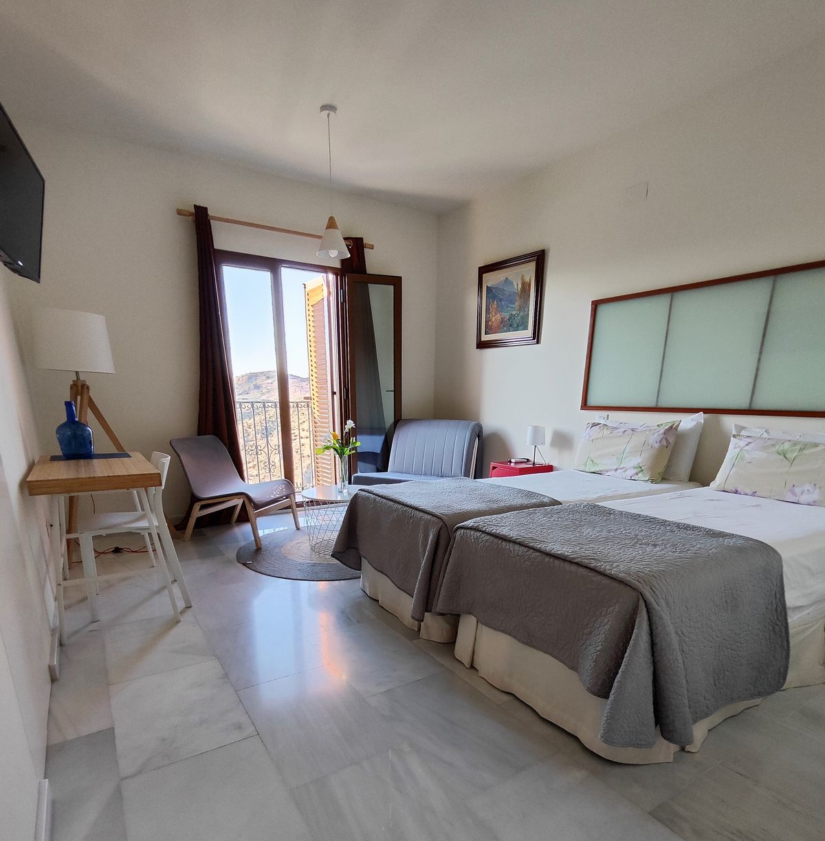 Habitación doble con dos camas individuales, escritorio y puerta al balcón con vistas a la sierra