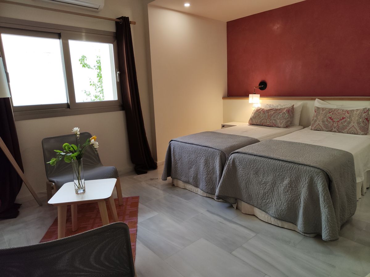 Habitación doble con dos camas individuales, pared granate y rincón de estar junto a la ventana