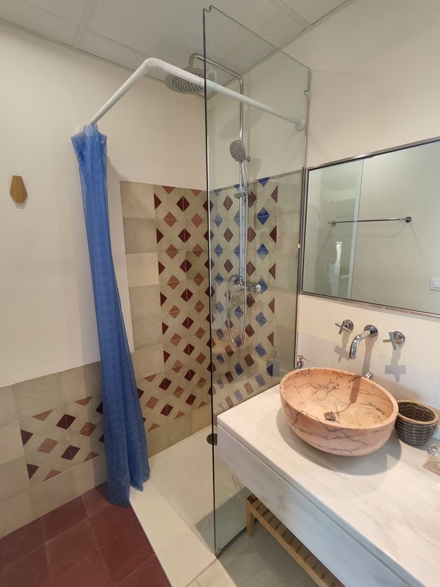 Baño de la suite con ducha, lavabo de piedra sobre mueble de madera y alicatado artesanal