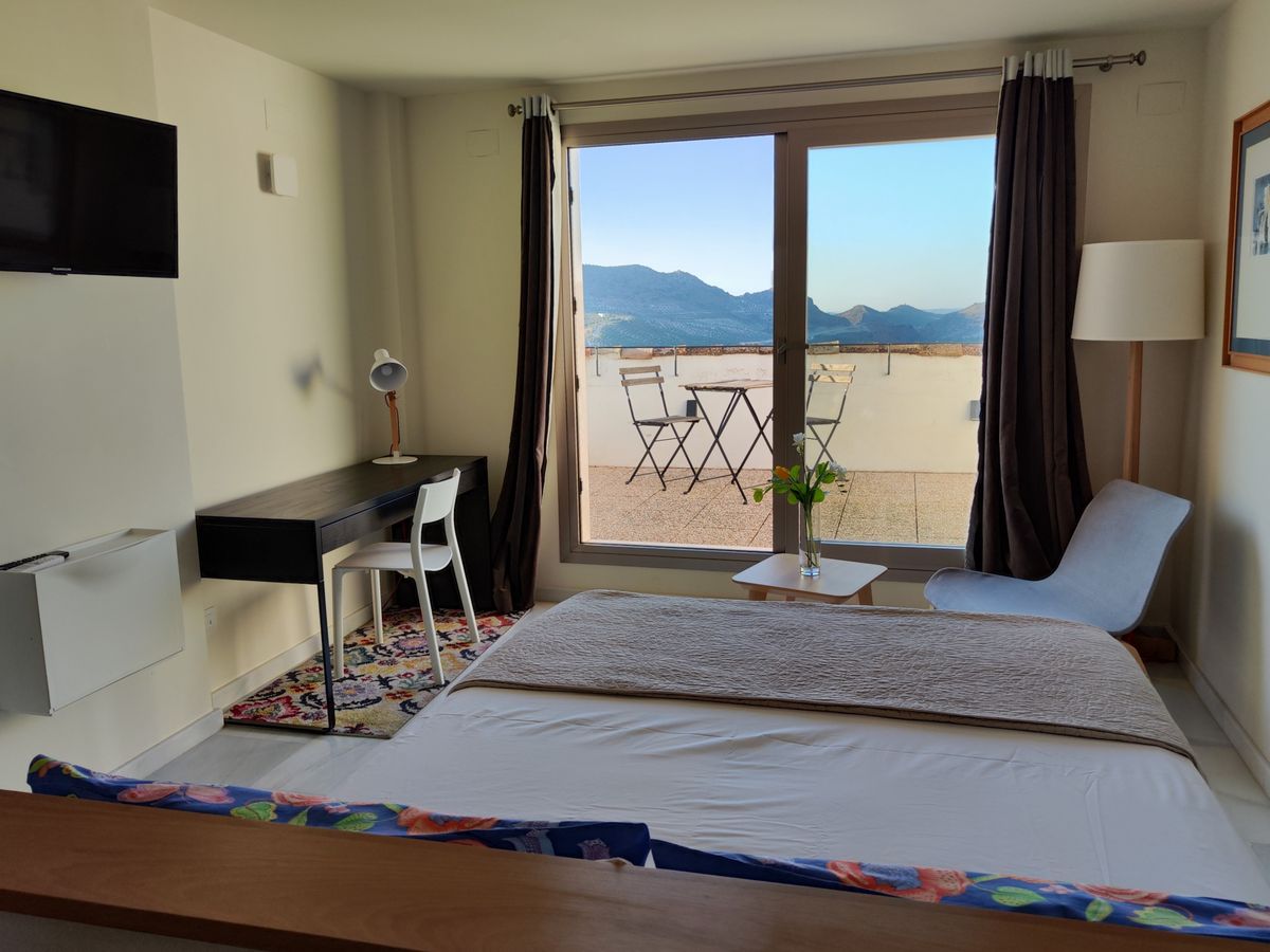 Dormitorio de la suite con cama de matrimonio y puerta de cristal a la terraza con vistas a la sierra