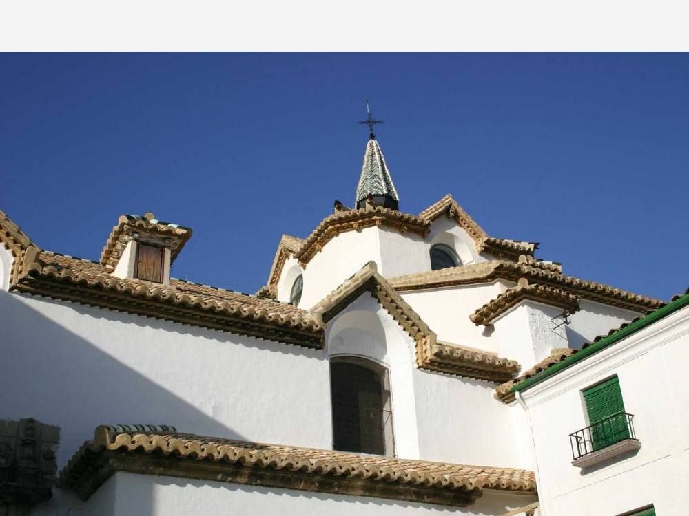 Fachada blanca de una iglesia con tejados de teja y remate de campanario bajo el cielo azul