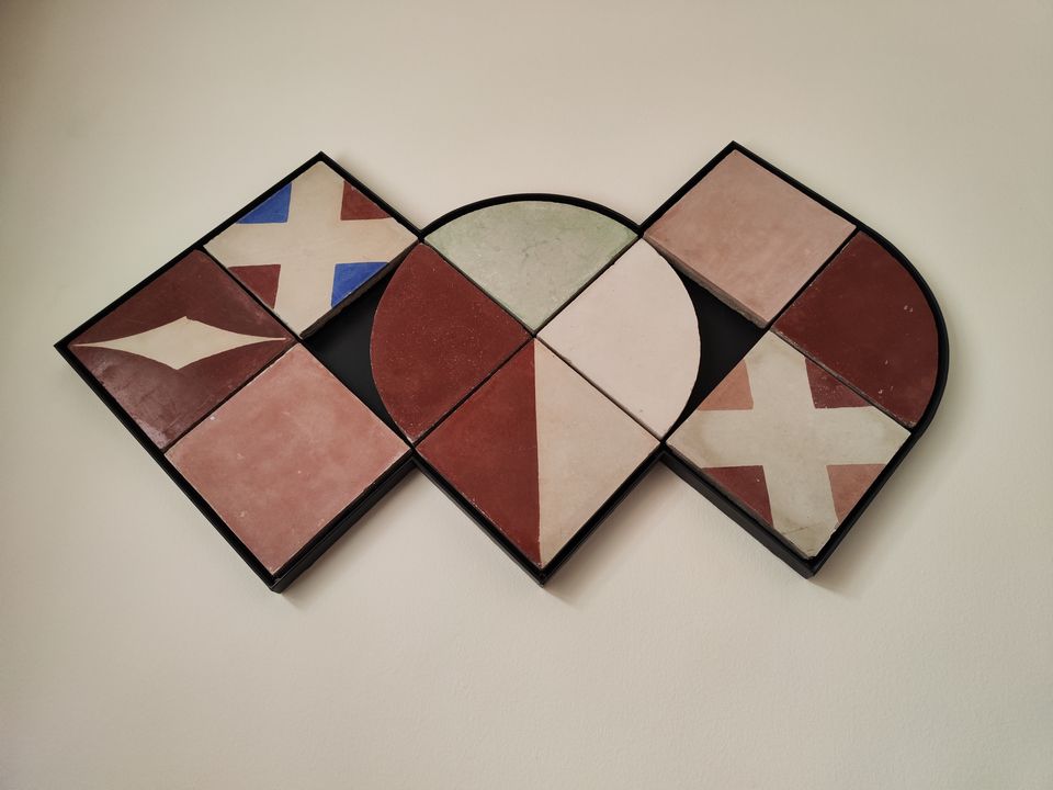 Composición mural hecha con piezas de baldosa hidráulica artesanal en tonos granate, azul y blanco