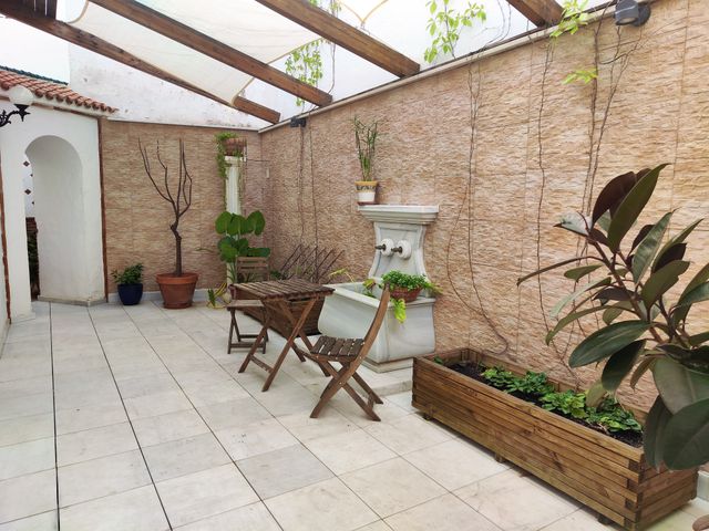 Patio andaluz con fuente de piedra, plantas, mesa con sillas y pérgola de madera