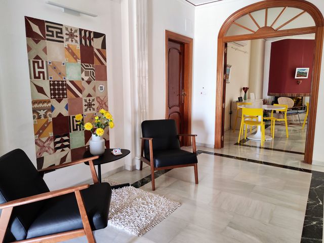 Recibidor con mural de baldosa hidráulica, butacas y un arco de madera que da al salón