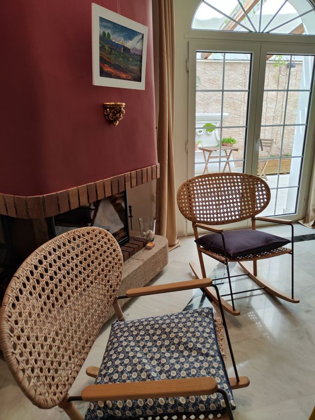 Rincón del salón con chimenea, mecedoras de mimbre y ventanal