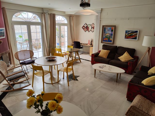 Salón de usos múltiples con sofás, mesa de comedor con sillas amarillas y ventanales en arco